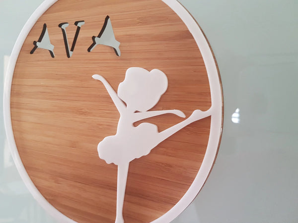 Round bamboo plaque with a white acrylic ballerina and the name Ava cut out
