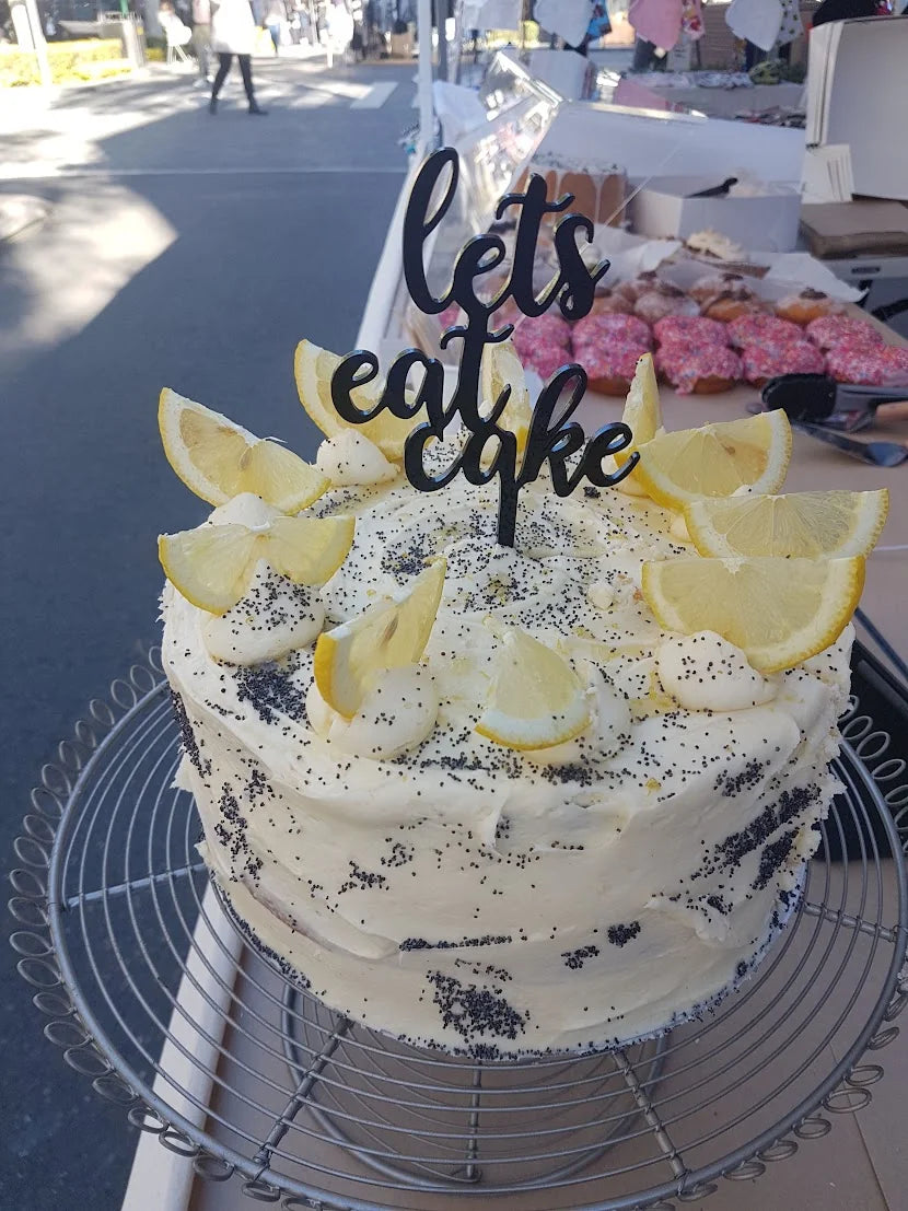 Black acrylic 'lets eat cake' cake topper on a lemon and poppy seed cake