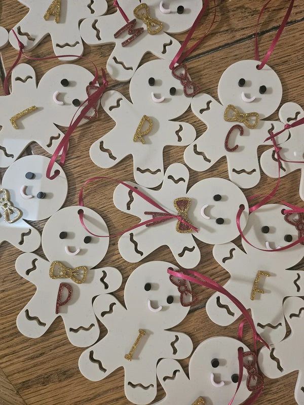 Pile of white acrylic gingerbread ornaments with gold bow ties and initials
