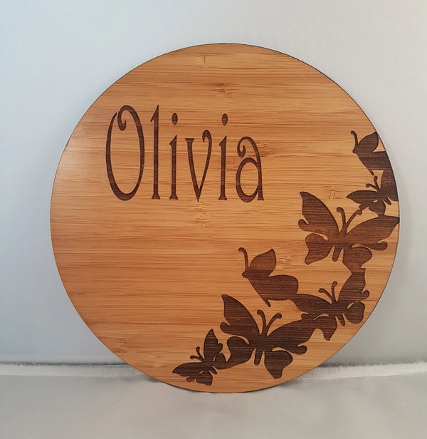 Round bamboo name plaque reading Olivia with engraved butterflies, front view