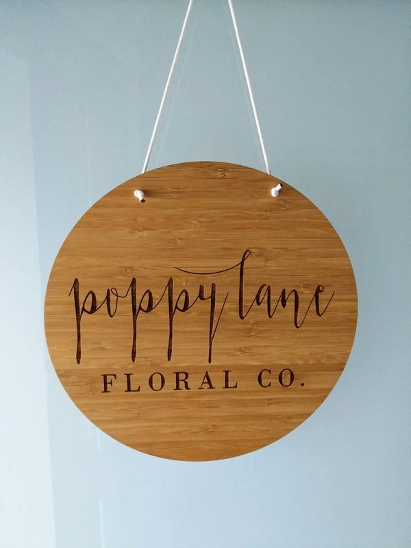 Round bamboo Poppy Lane Floral Co. sign hanging from white cord