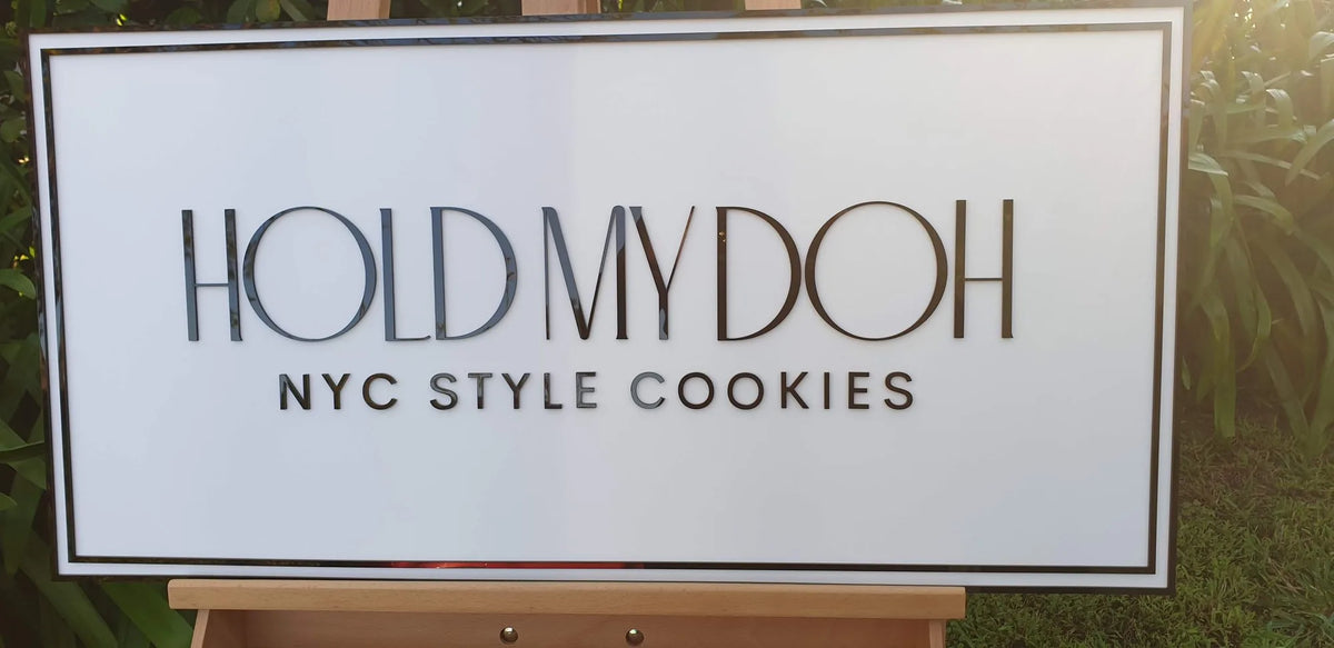 White rectangular Hold My Doh NYC Style Cookies sign with black acrylic lettering and border