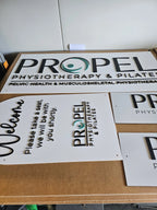 White Propel Physiotherapy and Pilates acrylic signs laid out on a workbench