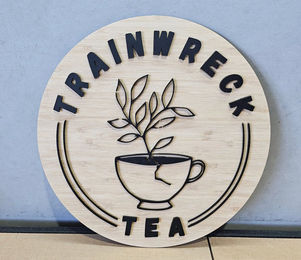 Round bamboo Trainwreck Tea sign with a teacup and plant